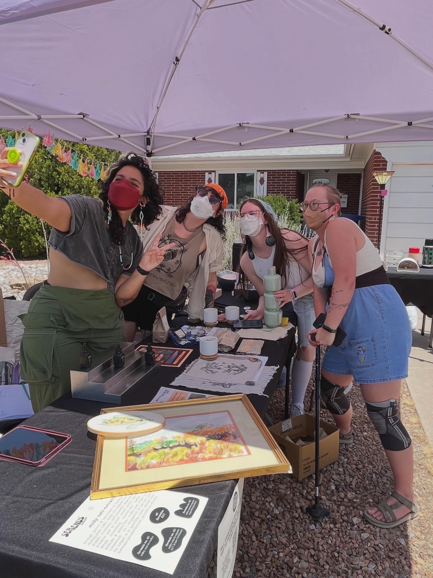 BTS pic of 4 friends posing together in a selfie, over/around a table of MPF perch and yard sale goodies. All 4 people are wearing K/N95 masks, one person is standing with a cane